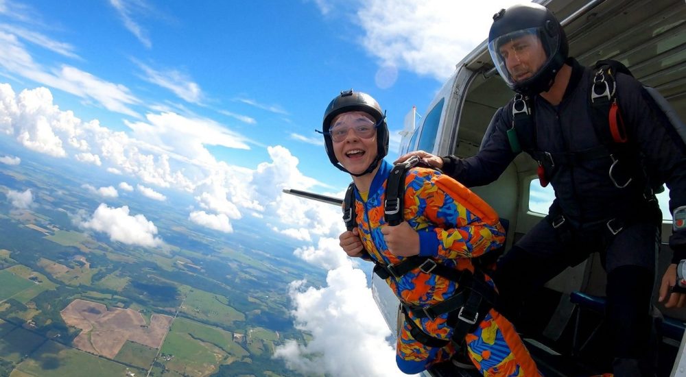 Un adolescent souriant et son instructeur sur le point de sauter en parachute depuis un avion au-dessus des nuages.