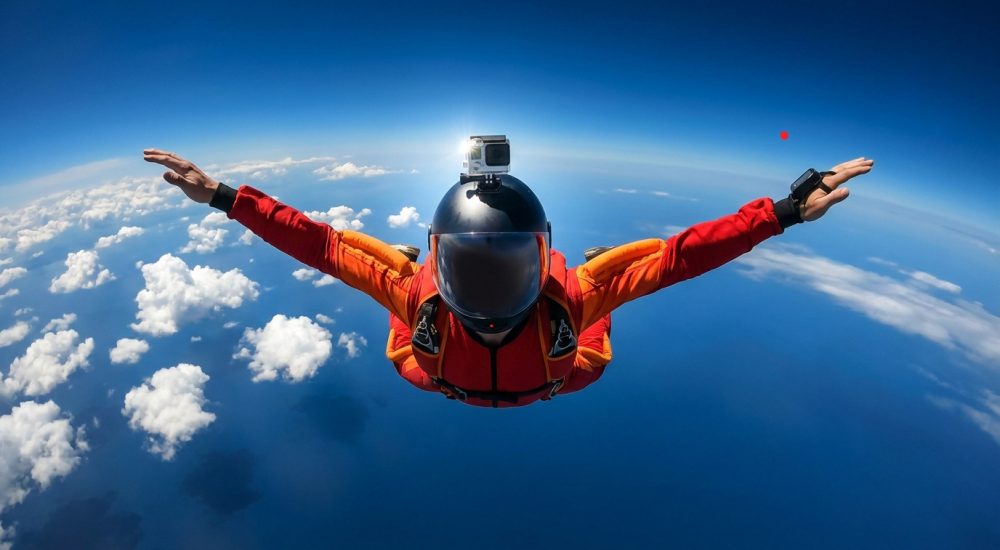 Parachutiste en combinaison rouge avec une caméra sur le casque en chute libre au-dessus des nuages.