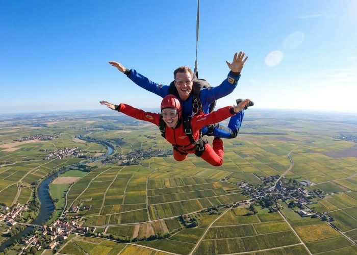 Un tandem de parachutistes souriants en chute libre au-dessus des vignobles et de la campagne champenoise.