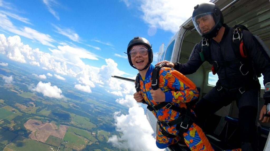 Un adolescent souriant et son instructeur sur le point de sauter en parachute depuis un avion au-dessus des nuages.